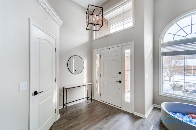 foyer with dark wood-type flooring, a notable chandelier, a towering ceiling, and baseboards