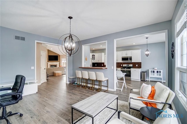 living room featuring a chandelier, a fireplace, wood finished floors, visible vents, and baseboards