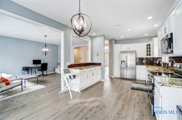 kitchen with decorative light fixtures, appliances with stainless steel finishes, glass insert cabinets, white cabinetry, and light stone countertops