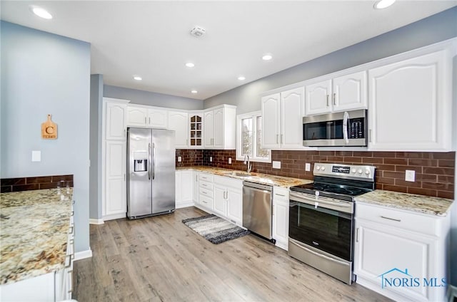 kitchen featuring appliances with stainless steel finishes, white cabinets, glass insert cabinets, and light stone countertops