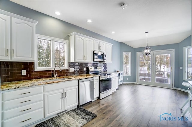 kitchen featuring light stone counters, decorative light fixtures, stainless steel appliances, white cabinetry, and a sink