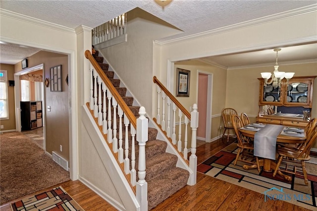 stairs with visible vents, ornamental molding, wood finished floors, a textured ceiling, and a notable chandelier