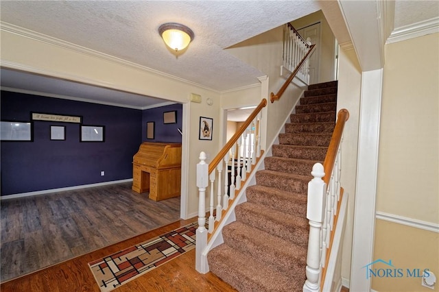 stairs featuring baseboards, a textured ceiling, ornamental molding, and wood finished floors