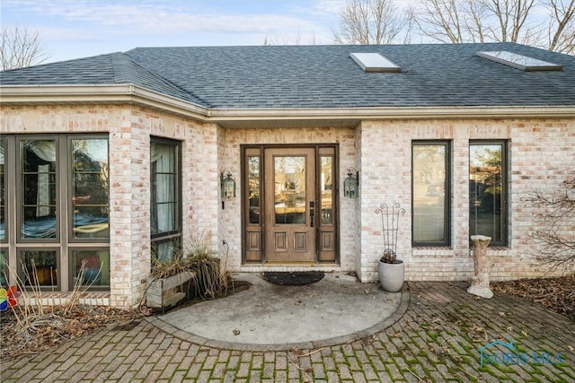 view of exterior entry featuring a shingled roof and brick siding