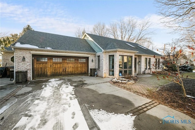 view of front of home with an attached garage, driveway, brick siding, and a shingled roof