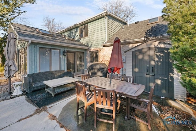 exterior space with an outbuilding, a patio, a shingled roof, brick siding, and a storage unit