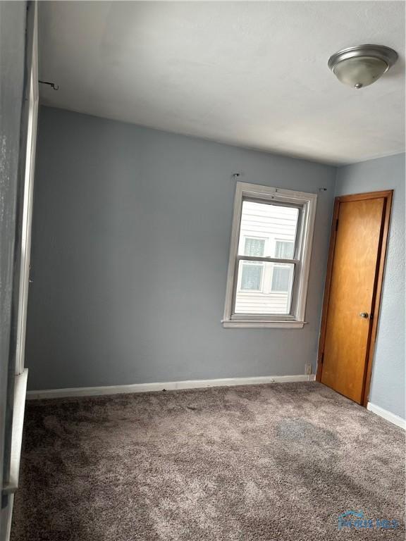 unfurnished room with baseboards and dark colored carpet