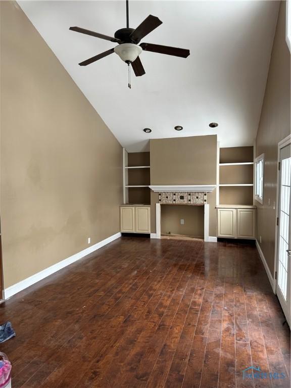 unfurnished living room with baseboards, dark wood-style floors, ceiling fan, built in shelves, and high vaulted ceiling