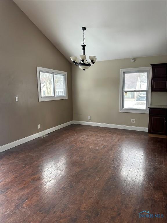 unfurnished room with dark wood finished floors, a notable chandelier, vaulted ceiling, and baseboards