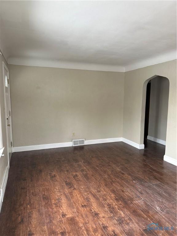 unfurnished room featuring baseboards, visible vents, arched walkways, and dark wood-style flooring