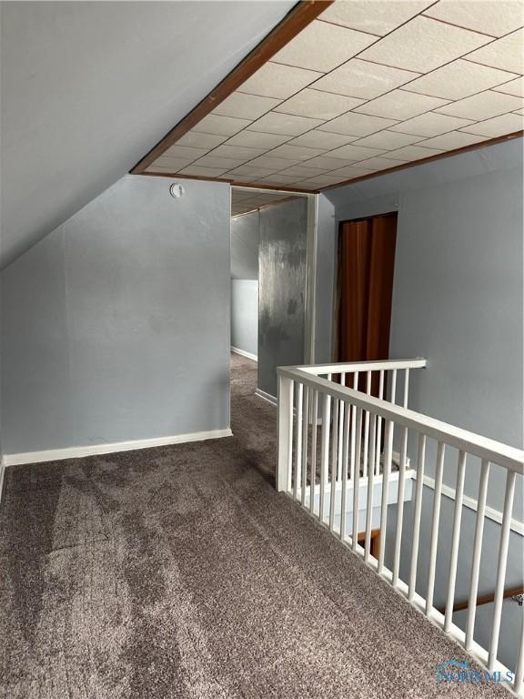 hallway with vaulted ceiling, dark colored carpet, and baseboards