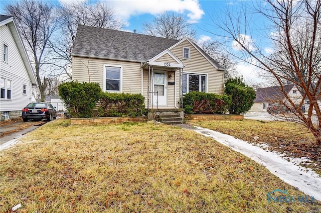 bungalow-style house with a shingled roof and a front lawn