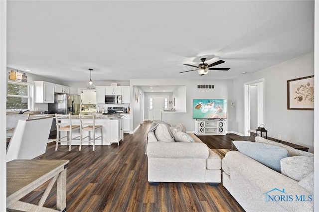 living room with baseboards, dark wood-type flooring, visible vents, and a ceiling fan