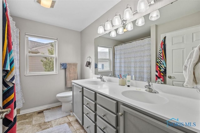 bathroom with baseboards, a sink, toilet, and double vanity