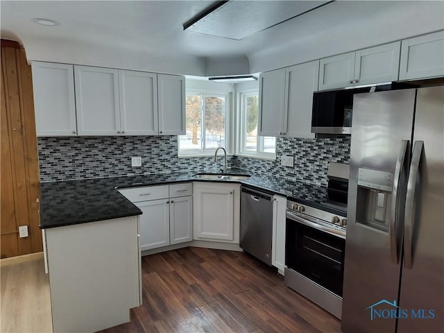 kitchen with dark wood-type flooring, decorative backsplash, white cabinets, stainless steel appliances, and a sink