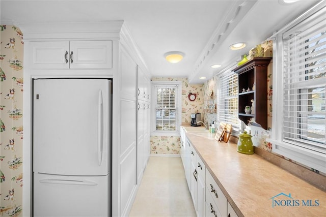 kitchen featuring white cabinets, baseboards, light countertops, freestanding refrigerator, and wallpapered walls