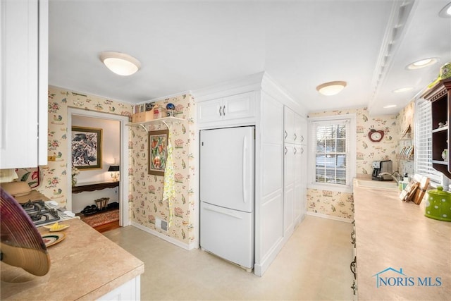 kitchen with light floors, light countertops, white cabinetry, white fridge, and wallpapered walls