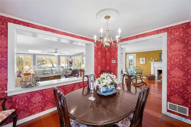 dining room featuring a warm lit fireplace, wood finished floors, visible vents, and wallpapered walls