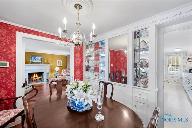 dining area featuring a lit fireplace, ornamental molding, an inviting chandelier, and wallpapered walls