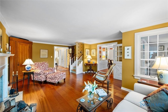 living area featuring a fireplace with raised hearth, ornamental molding, wood finished floors, and stairs