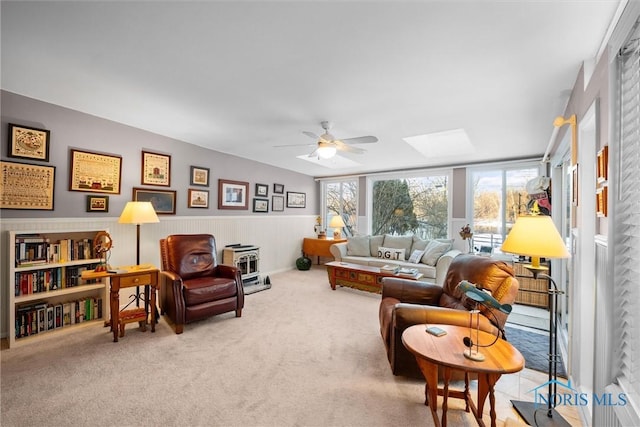 interior space featuring a skylight, carpet flooring, a ceiling fan, wainscoting, and a wood stove