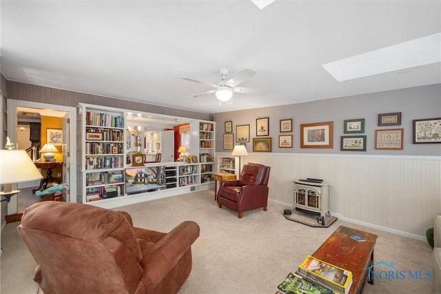 living area featuring carpet, ceiling fan, a skylight, and a wood stove