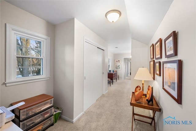 corridor featuring light colored carpet, vaulted ceiling, and baseboards