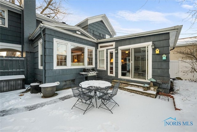 snow covered patio featuring outdoor dining area, area for grilling, and fence