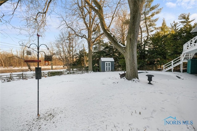 yard layered in snow featuring a shed, stairway, and an outbuilding