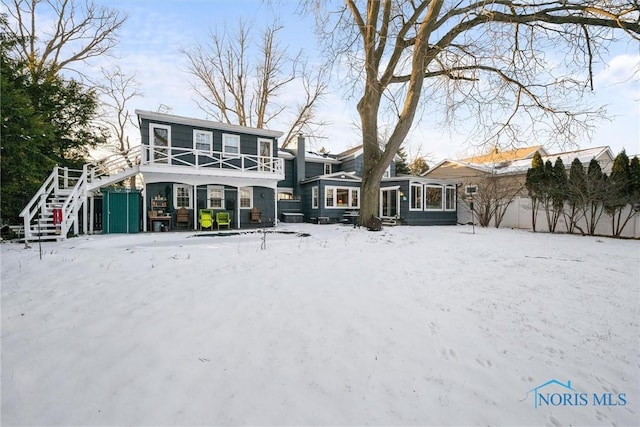 snow covered house featuring a chimney, a sunroom, and stairway