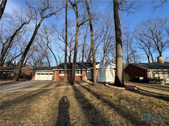 ranch-style home featuring aphalt driveway, a garage, brick siding, and a chimney