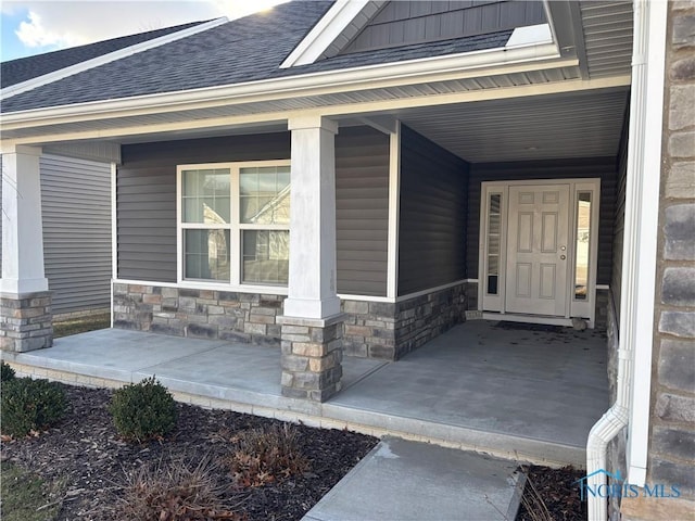 entrance to property featuring stone siding, covered porch, roof with shingles, and a carport