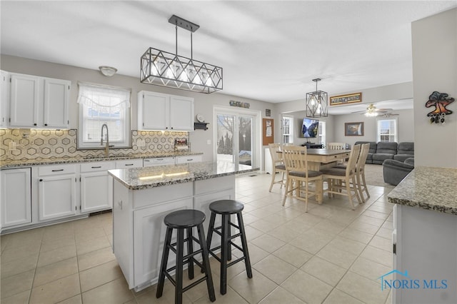 kitchen featuring hanging light fixtures, backsplash, light tile patterned flooring, a sink, and white cabinetry