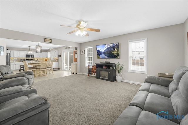 living area featuring a fireplace, baseboards, a ceiling fan, and light colored carpet