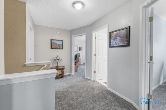 hallway with carpet flooring, a textured wall, a textured ceiling, and baseboards