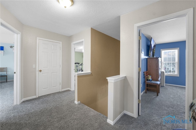 hallway featuring carpet, baseboards, a textured ceiling, and an upstairs landing