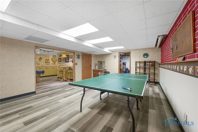 recreation room with wallpapered walls, baseboards, a drop ceiling, and wood finished floors