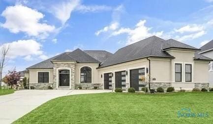 french country home with a garage, stone siding, concrete driveway, and a front yard