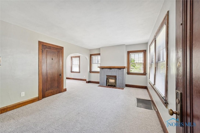 unfurnished living room with arched walkways, visible vents, light carpet, and baseboards