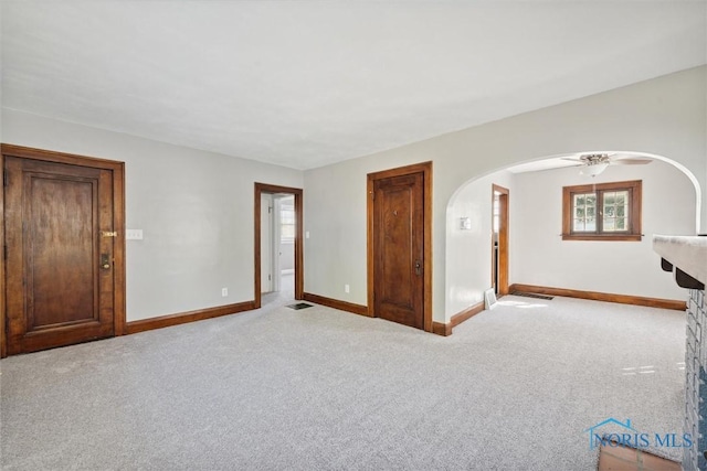 unfurnished room with arched walkways, light carpet, ceiling fan, and baseboards