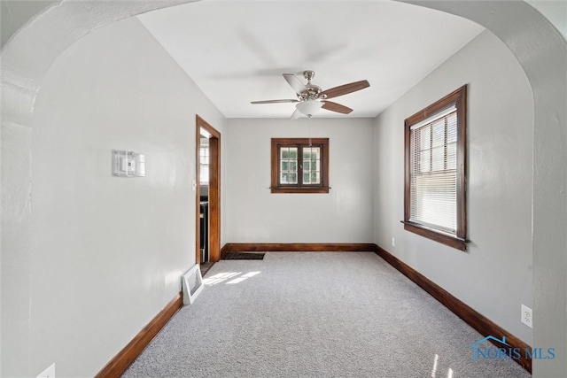 empty room featuring arched walkways, light carpet, visible vents, and baseboards