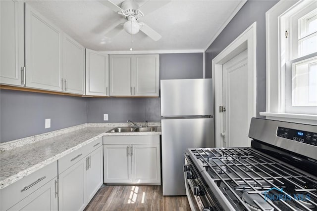 kitchen with appliances with stainless steel finishes, wood finished floors, light stone countertops, white cabinetry, and a sink