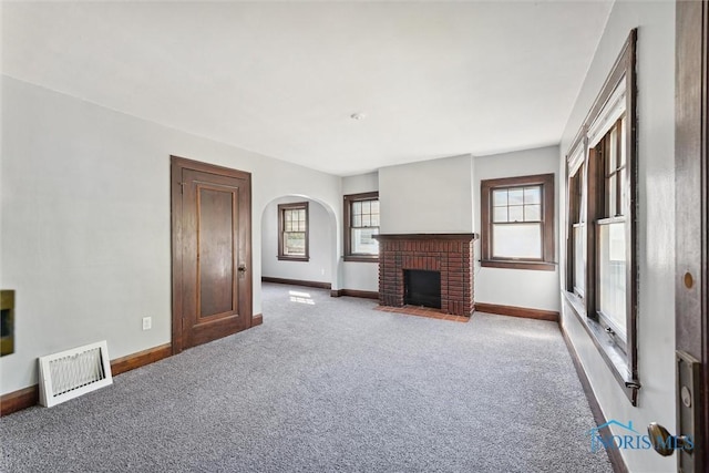 unfurnished living room featuring arched walkways, carpet flooring, visible vents, baseboards, and a brick fireplace