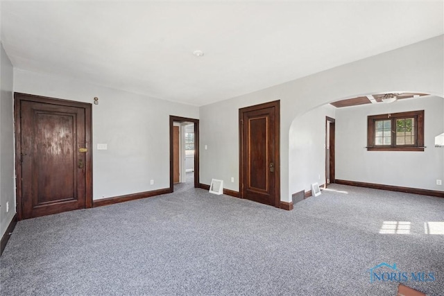 carpeted spare room with arched walkways, visible vents, and baseboards