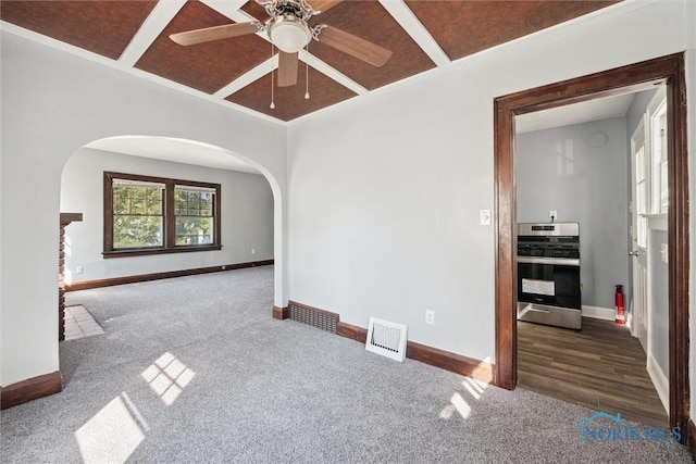 spare room featuring arched walkways, a ceiling fan, visible vents, baseboards, and dark colored carpet