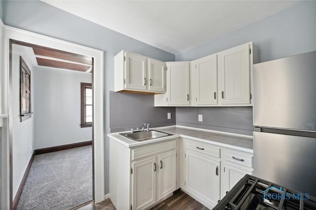 kitchen featuring a sink, white cabinets, light countertops, freestanding refrigerator, and dark colored carpet