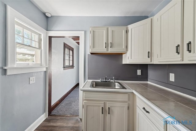 kitchen featuring dark wood-style floors, white cabinetry, a sink, and baseboards