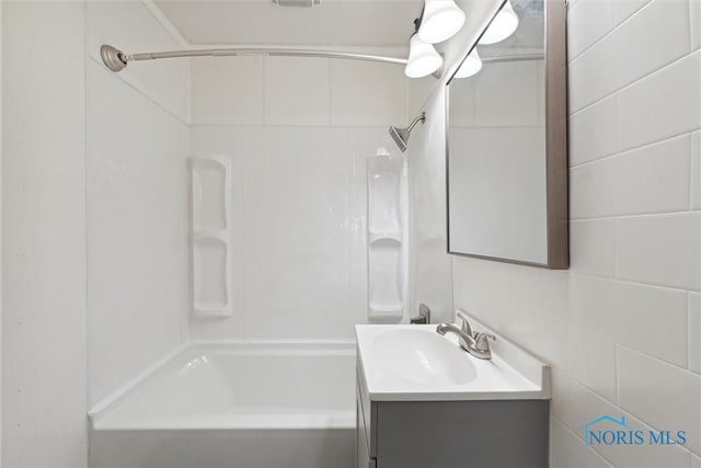 full bath featuring washtub / shower combination, vanity, and tile walls