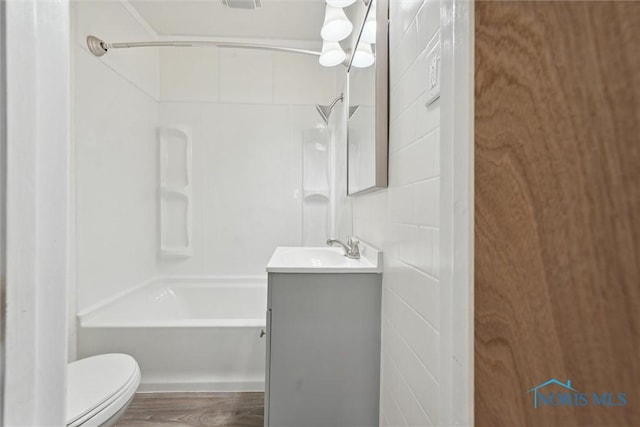 bathroom with tile walls, bathing tub / shower combination, toilet, vanity, and wood finished floors