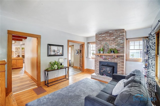 living room featuring light wood-style floors, a wood stove, plenty of natural light, and baseboards